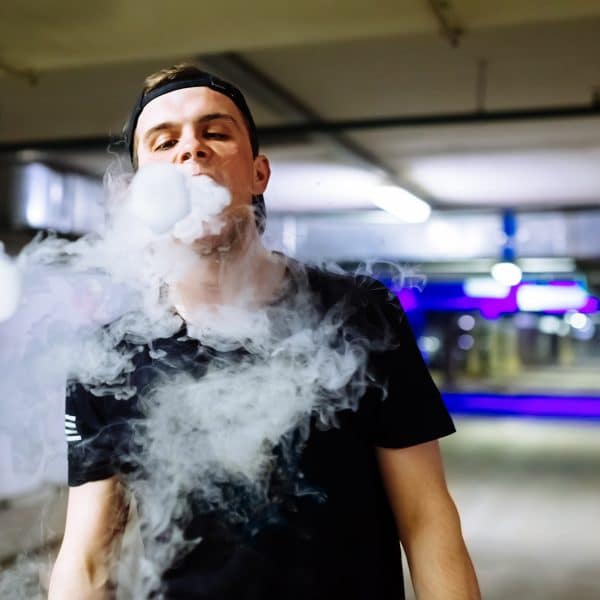 Man in cap smoke an electronic cigarette performing various kind of vaping tricks